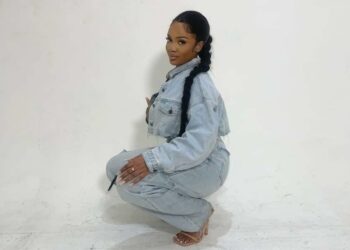 NKTA is pictured crouching, wearing denim, with a long ponytail over one shoulder.