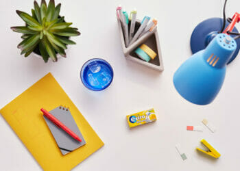 Picture shows a desk populated with a oencil case, lamp, notbooks, and a packet of Wrigley's Extra chewing gum.
